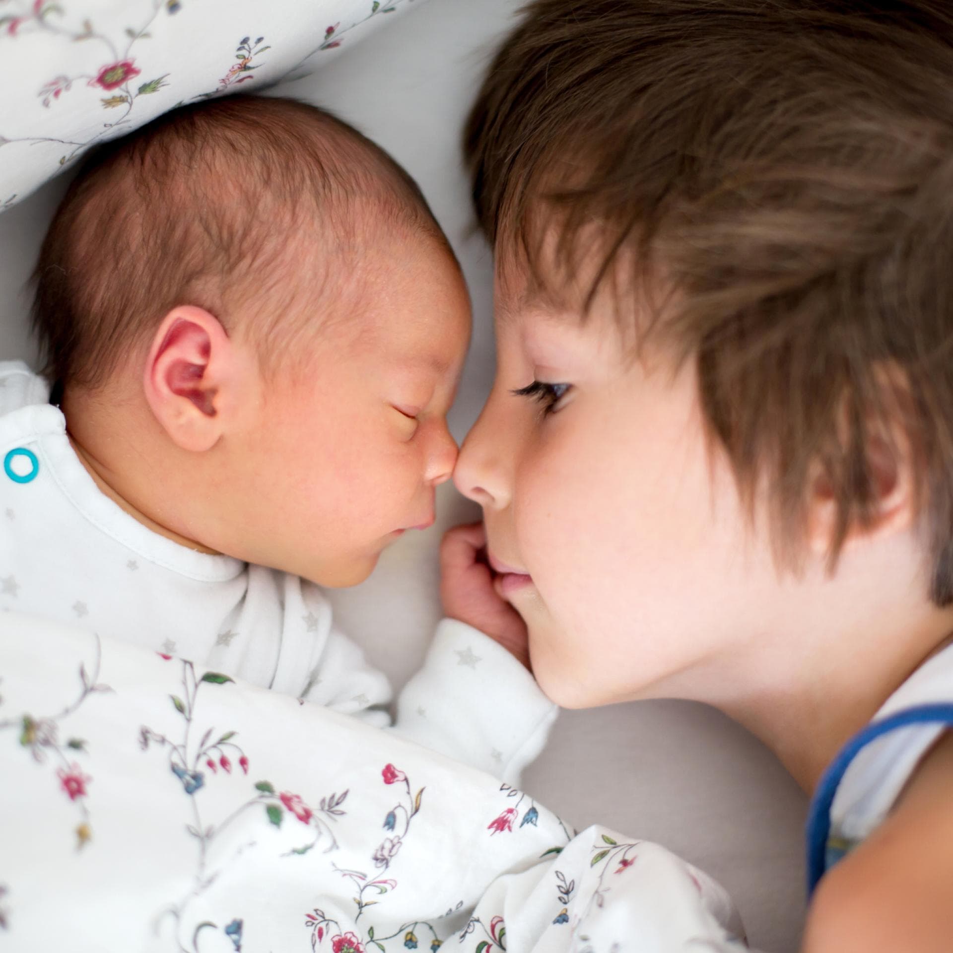 Großer Bruder liegt neben Baby im Bett.
