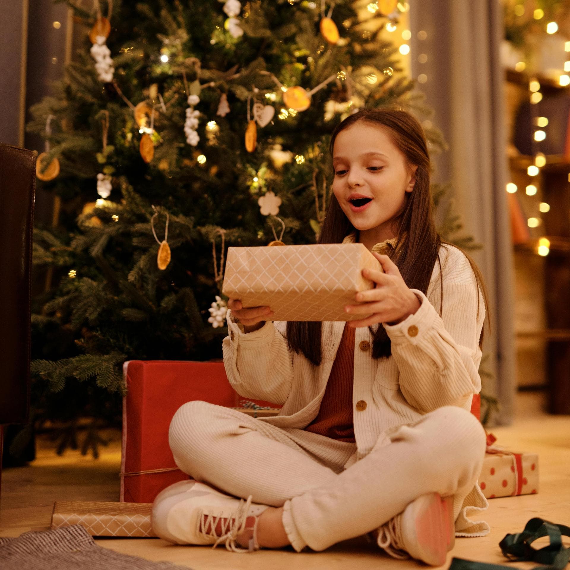 Ein Mädchen sitzt vor em Weihnachtsbaum und freut sich über ihr Geschenk.
