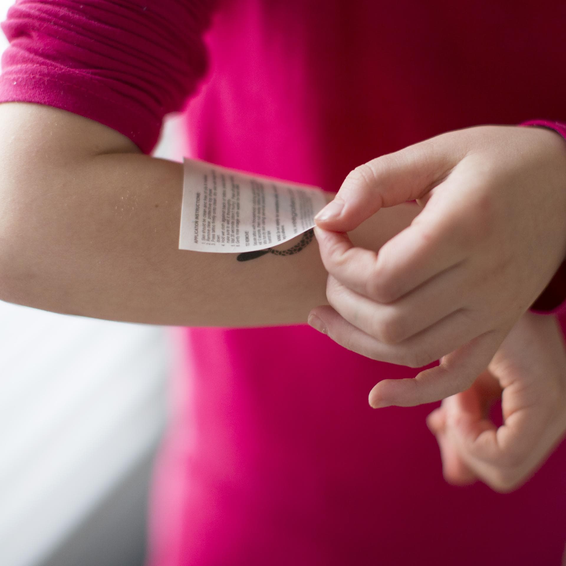 Kind klebt sich ein Tattoo auf den Arm.