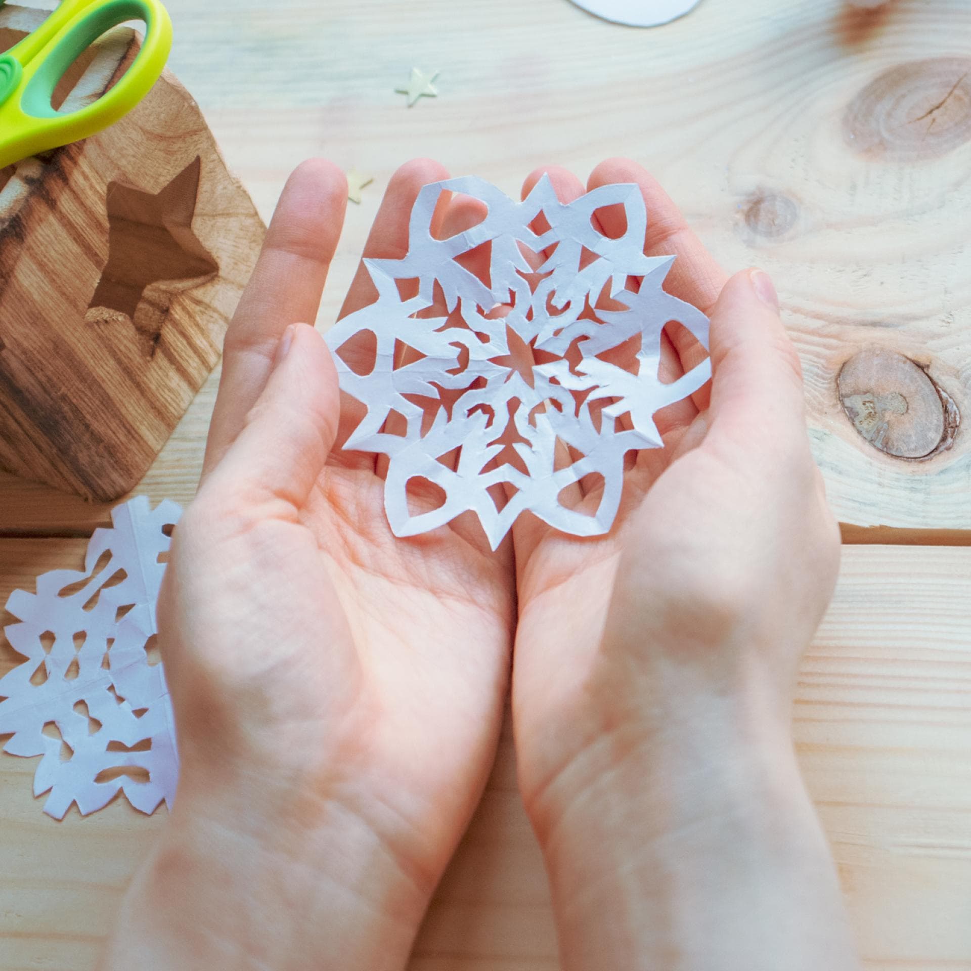 Kind hält selbst gebastelte Schneeflocke in der Hand.