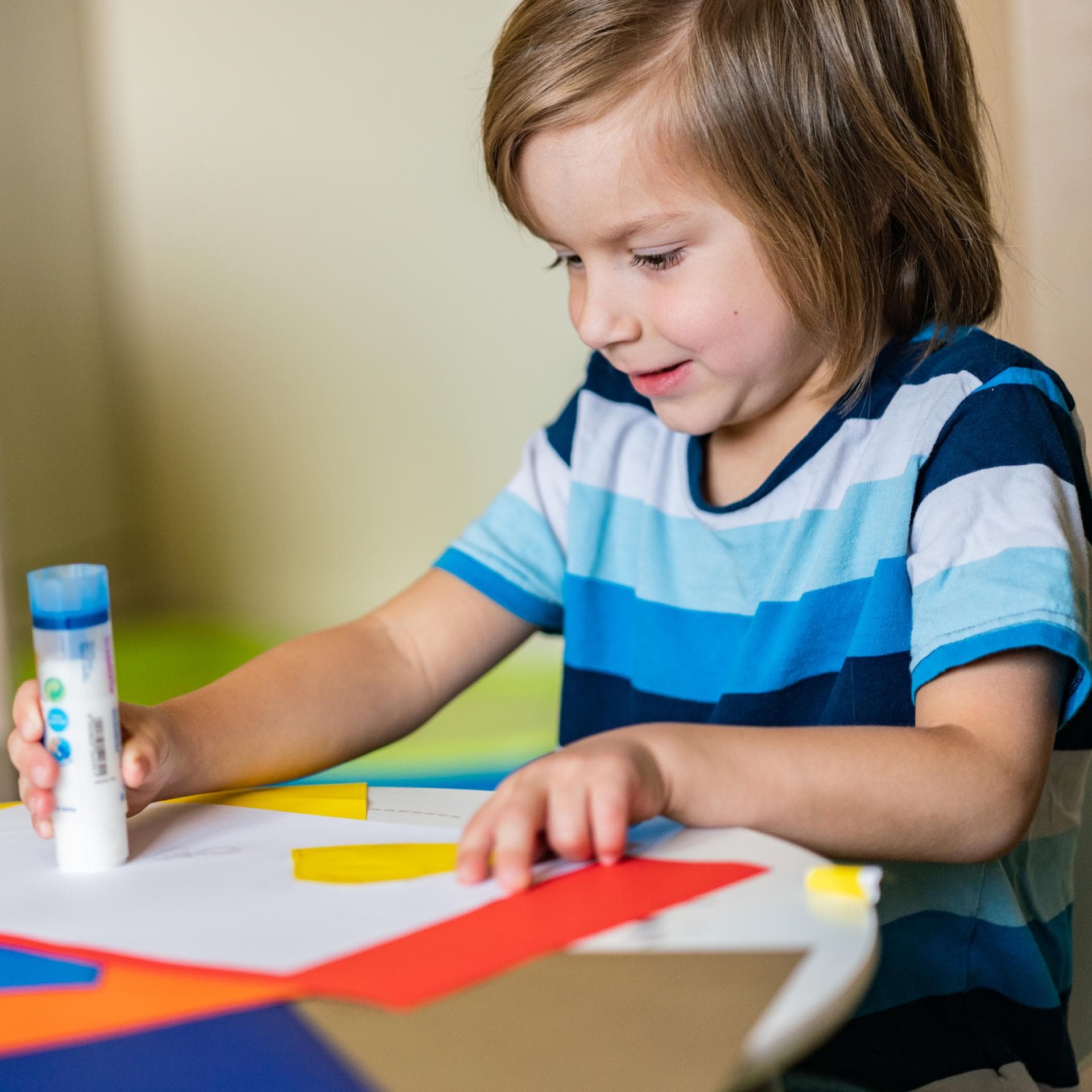 Kind mit Klebestift und buntem Papier.