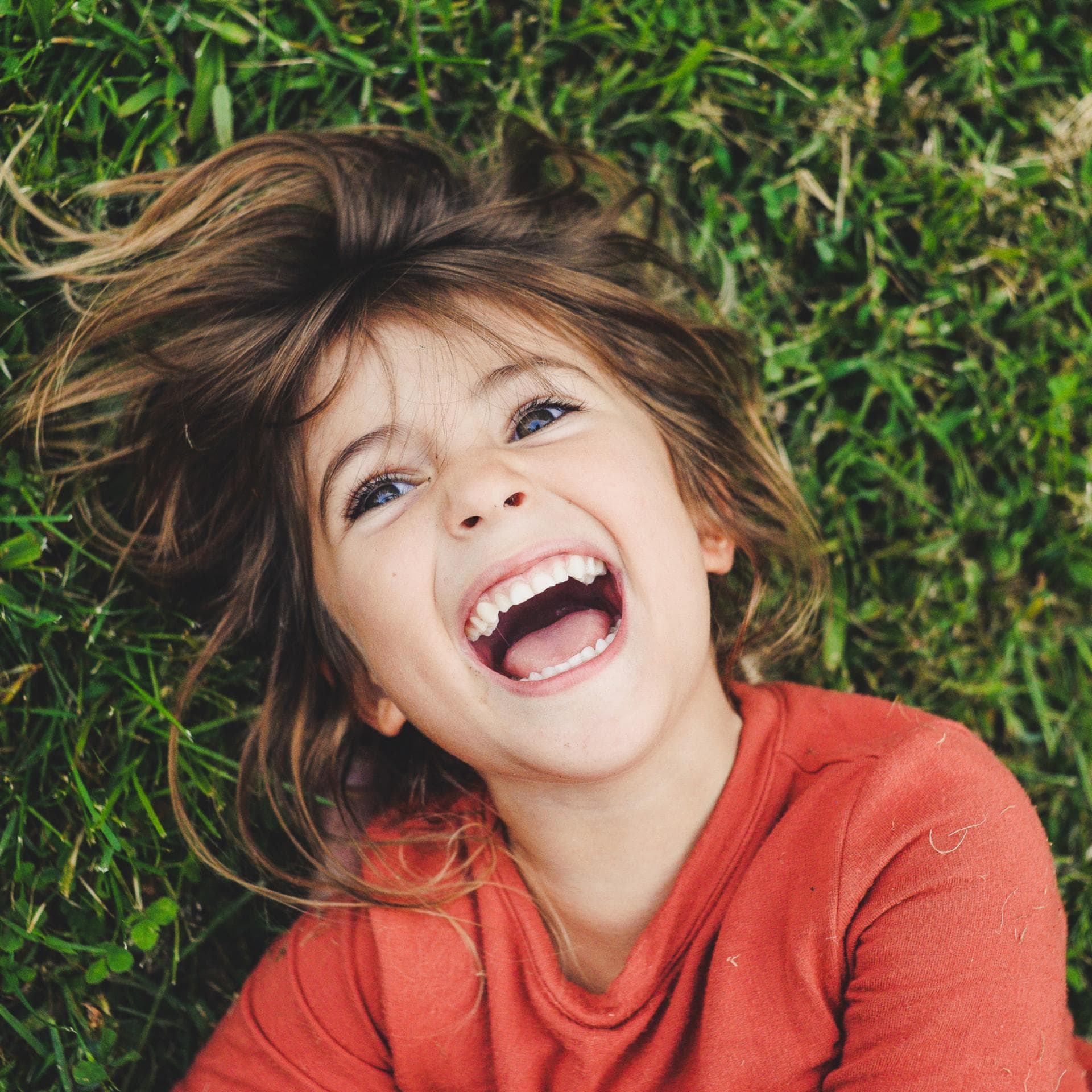 Ein Mädchen, das im Gras liegt und lacht.