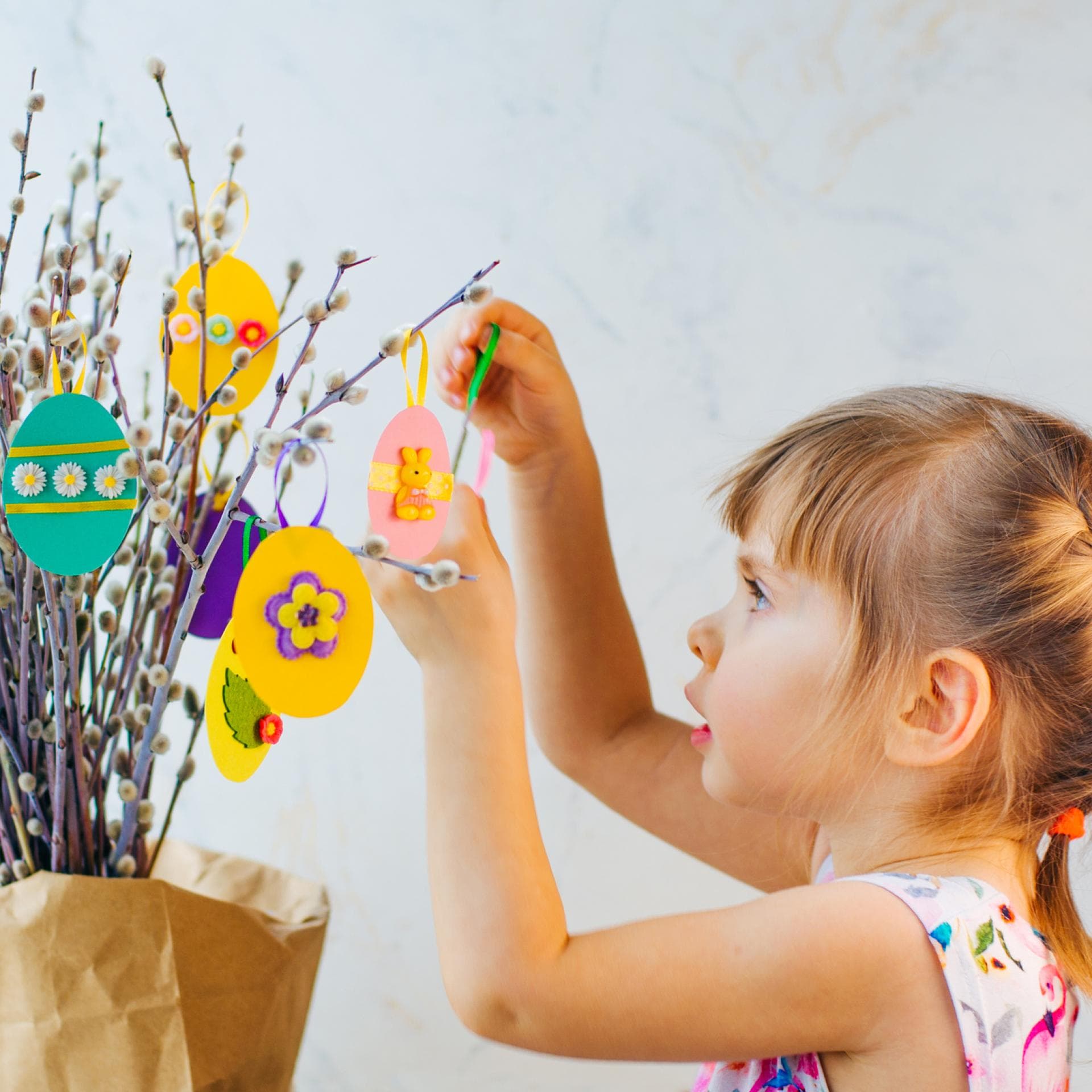Kleines Mädchen hängt selbst gebastelte Ostereier an den Strauch.