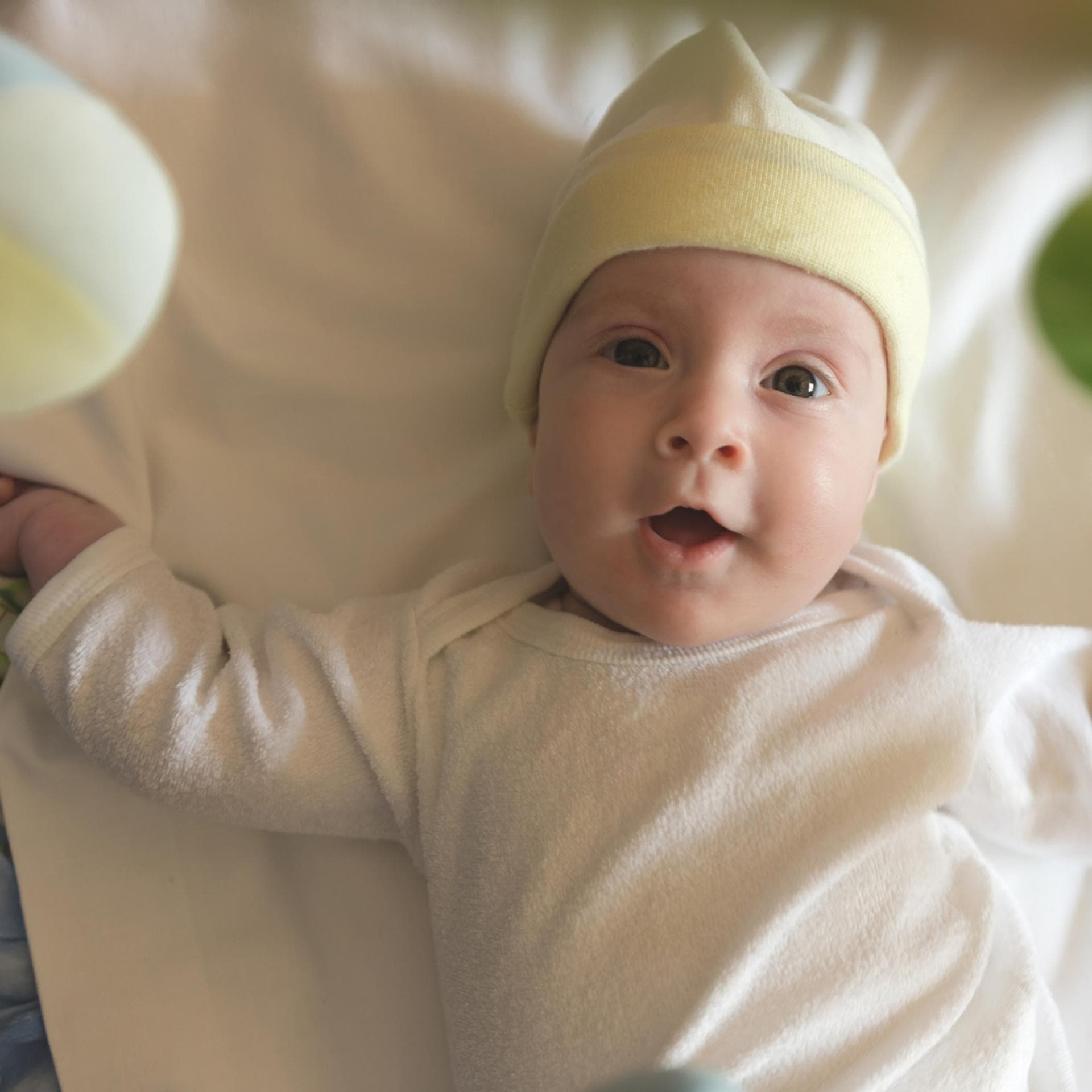 Baby liegt fröhlich unter einem Mobile.