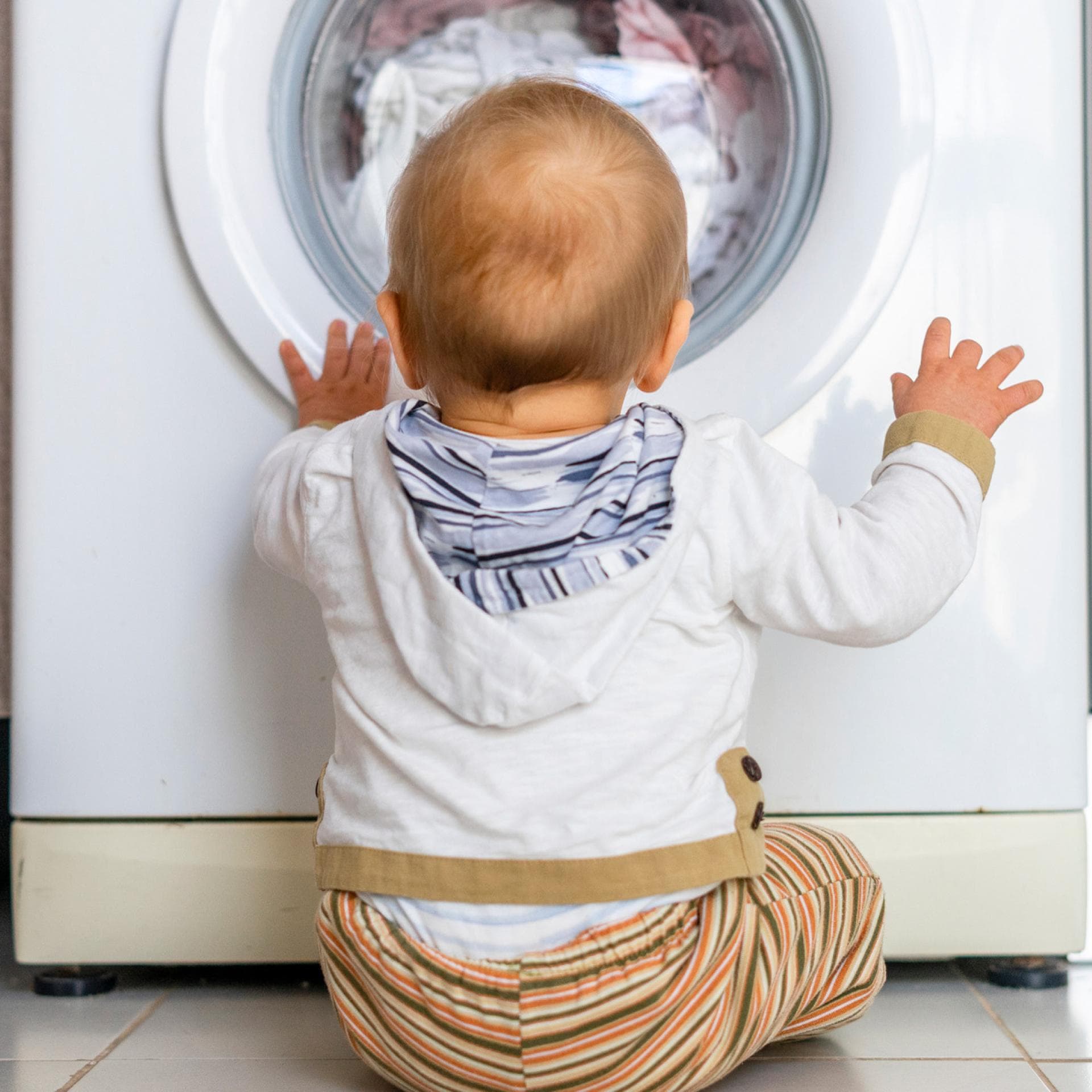 Baby sitzt vor der Waschmaschine und schaut hinein.