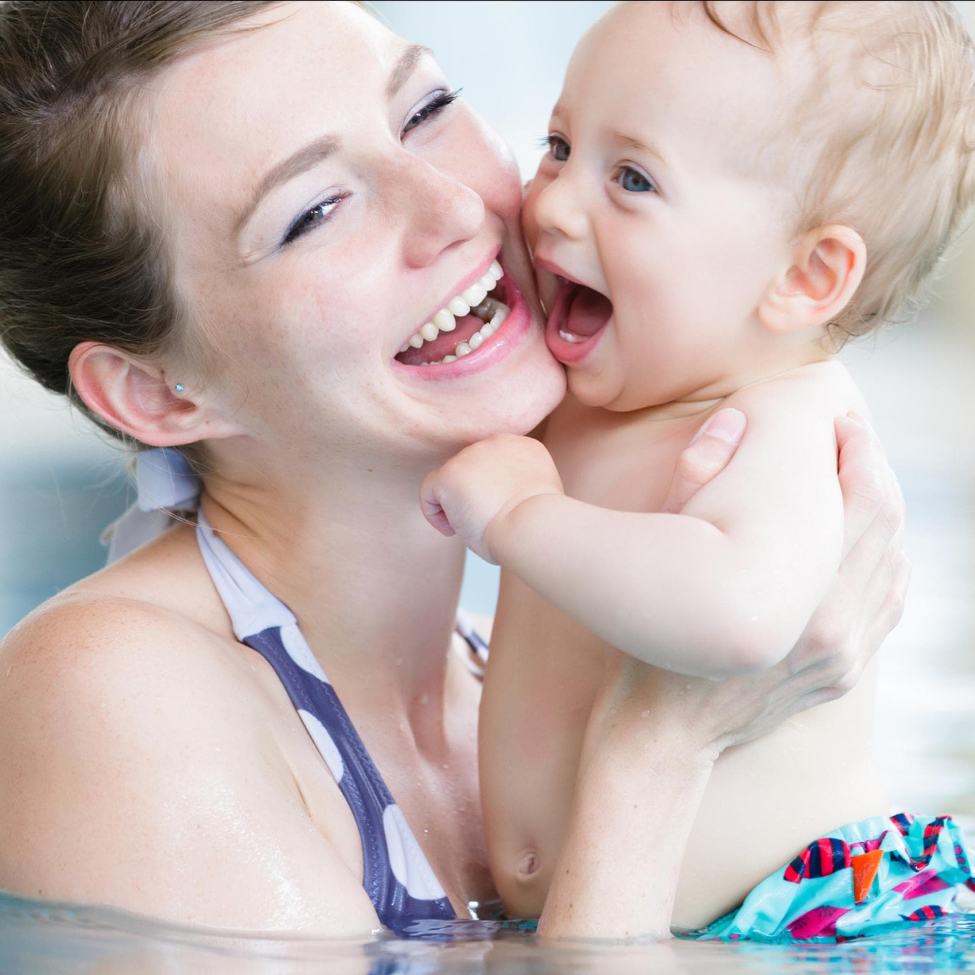 Ein Baby in Schwimmwindeln plantscht mit seiner Mutter im Schwimmbad. 