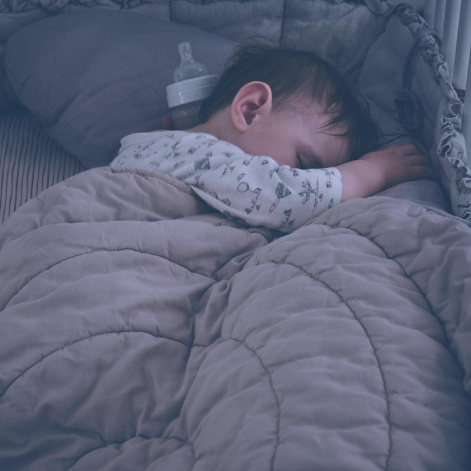 Baby im Bett mit Nestchen und Decke.
