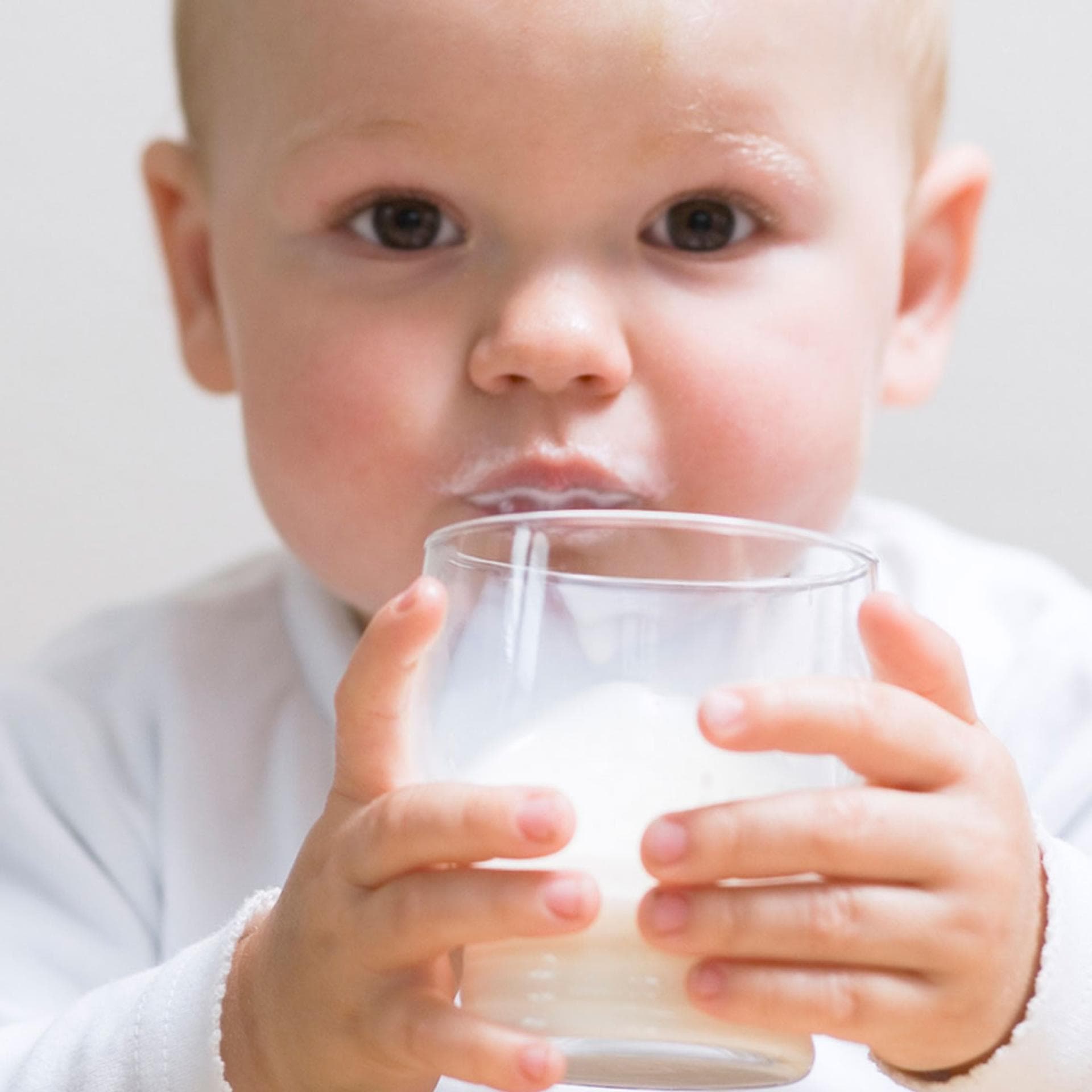 Kleinkind trinkt Milch aus dem Glas.