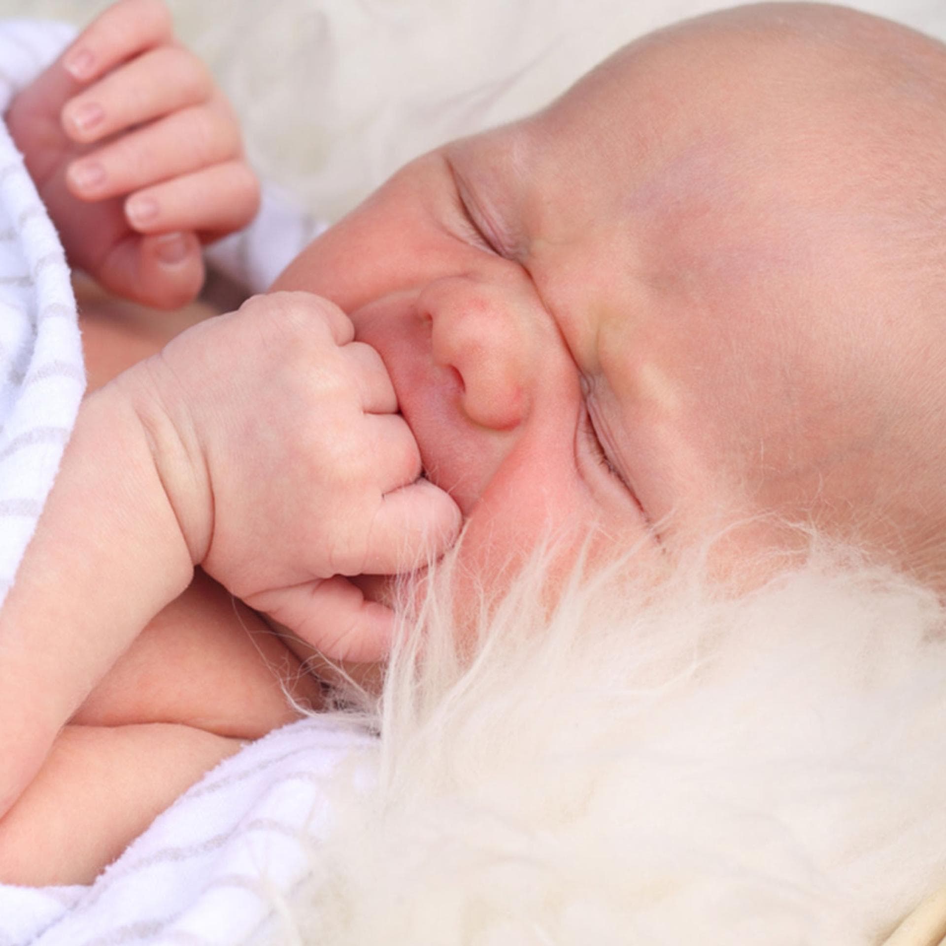 Baby liegt bei sommrlichen Temperaturen auf einem Lammfell
