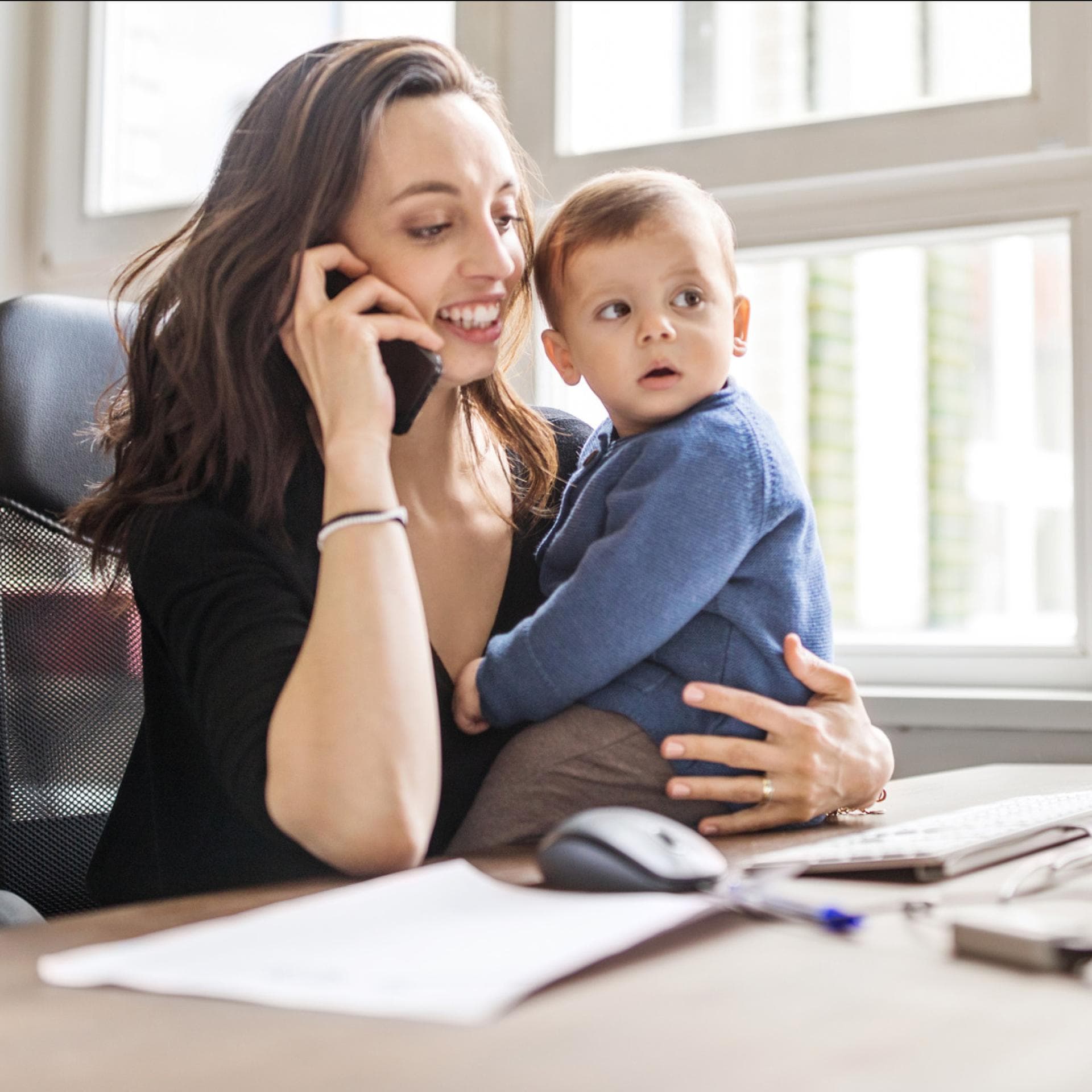 Mutter arbeitet mit Kind auf dem Schoß.