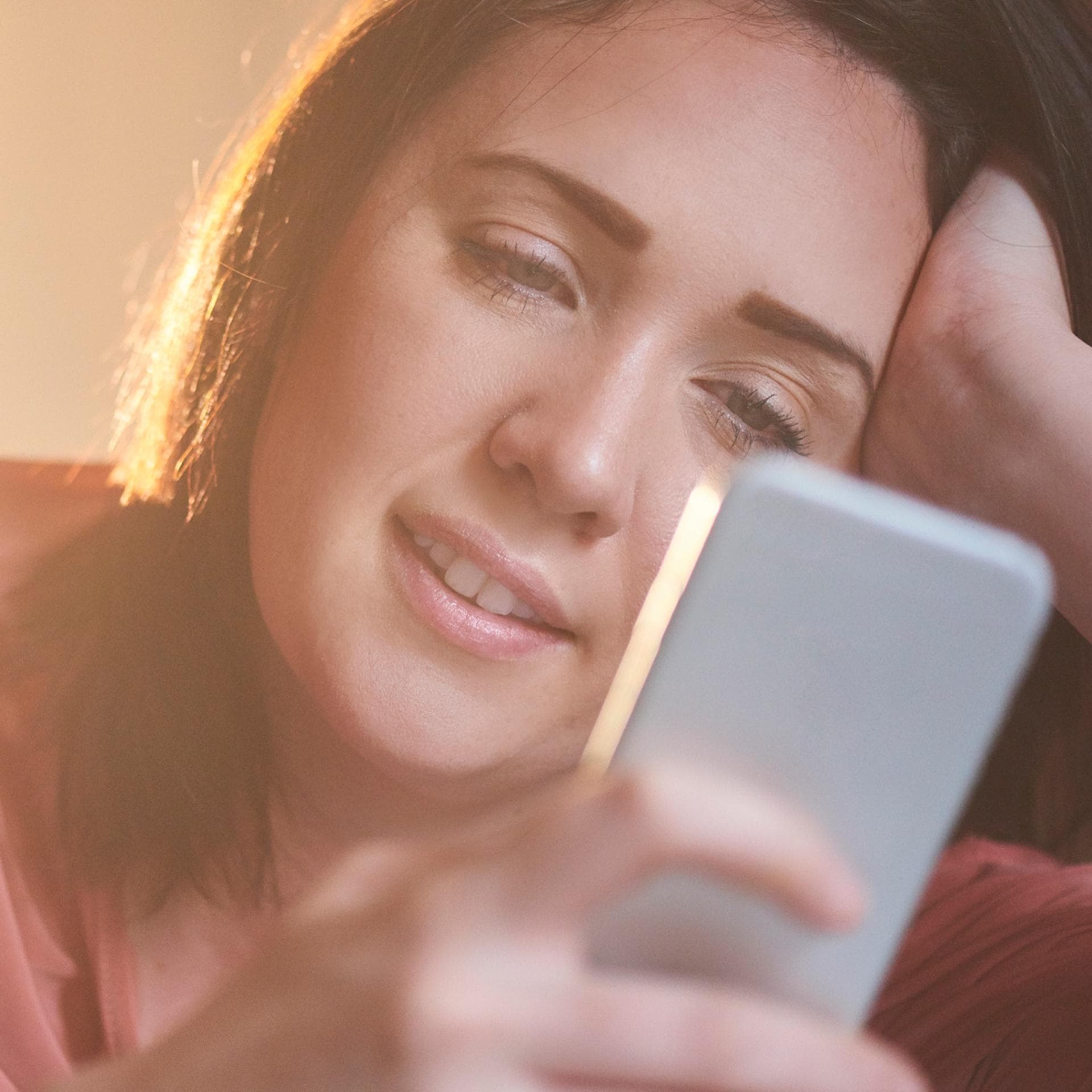 Frau lächelt, während sie auf ihr Smartphone schaut.