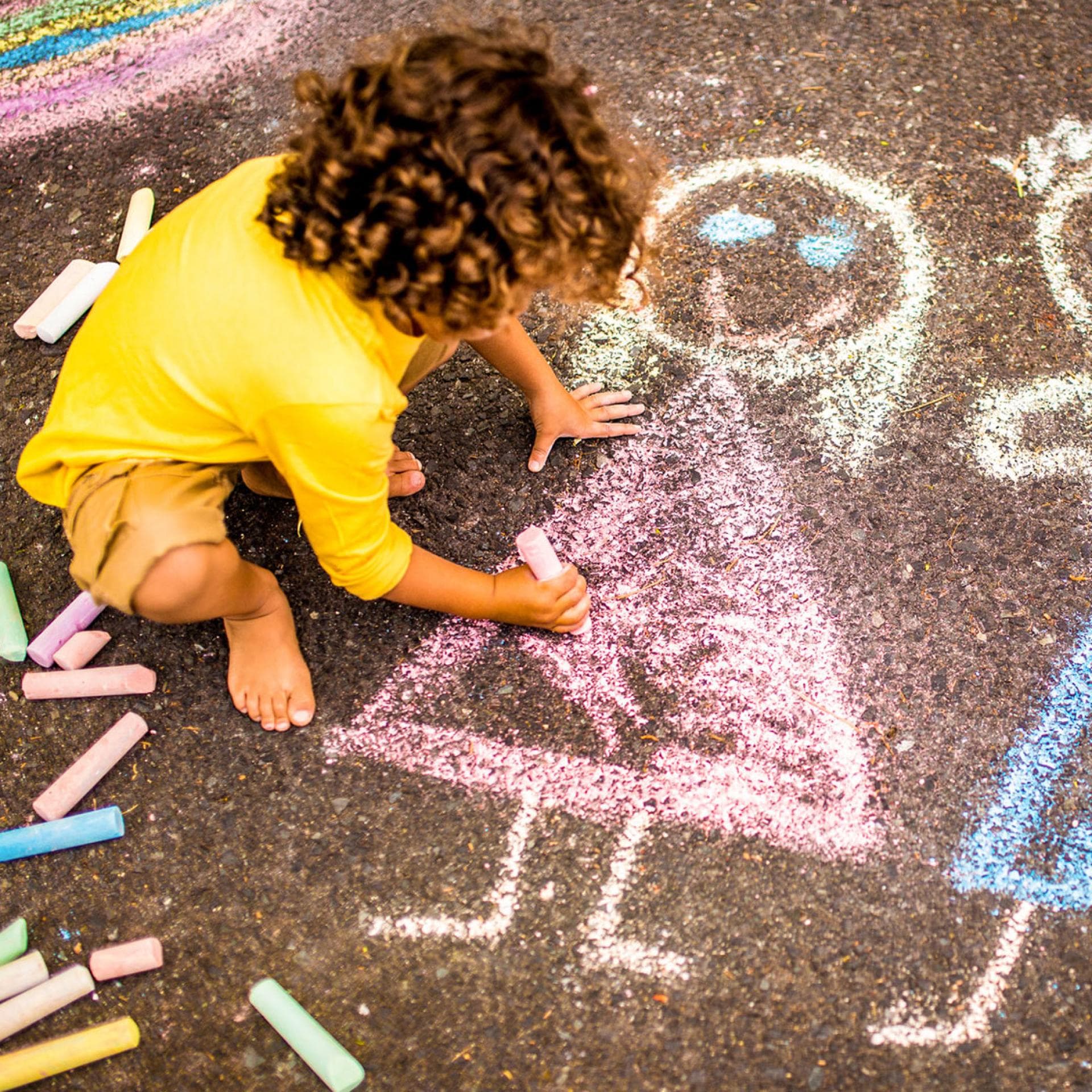 Kind malt mit Straßenmalkreide.