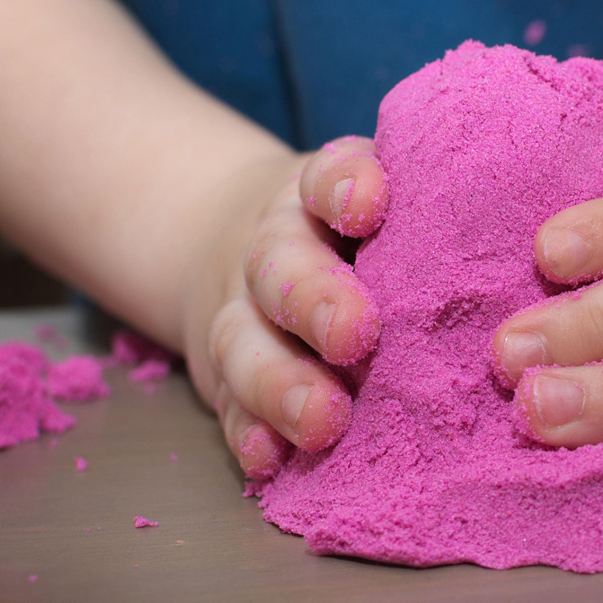 Kinderhände mit pinkfarbenem Kinetic Sand.