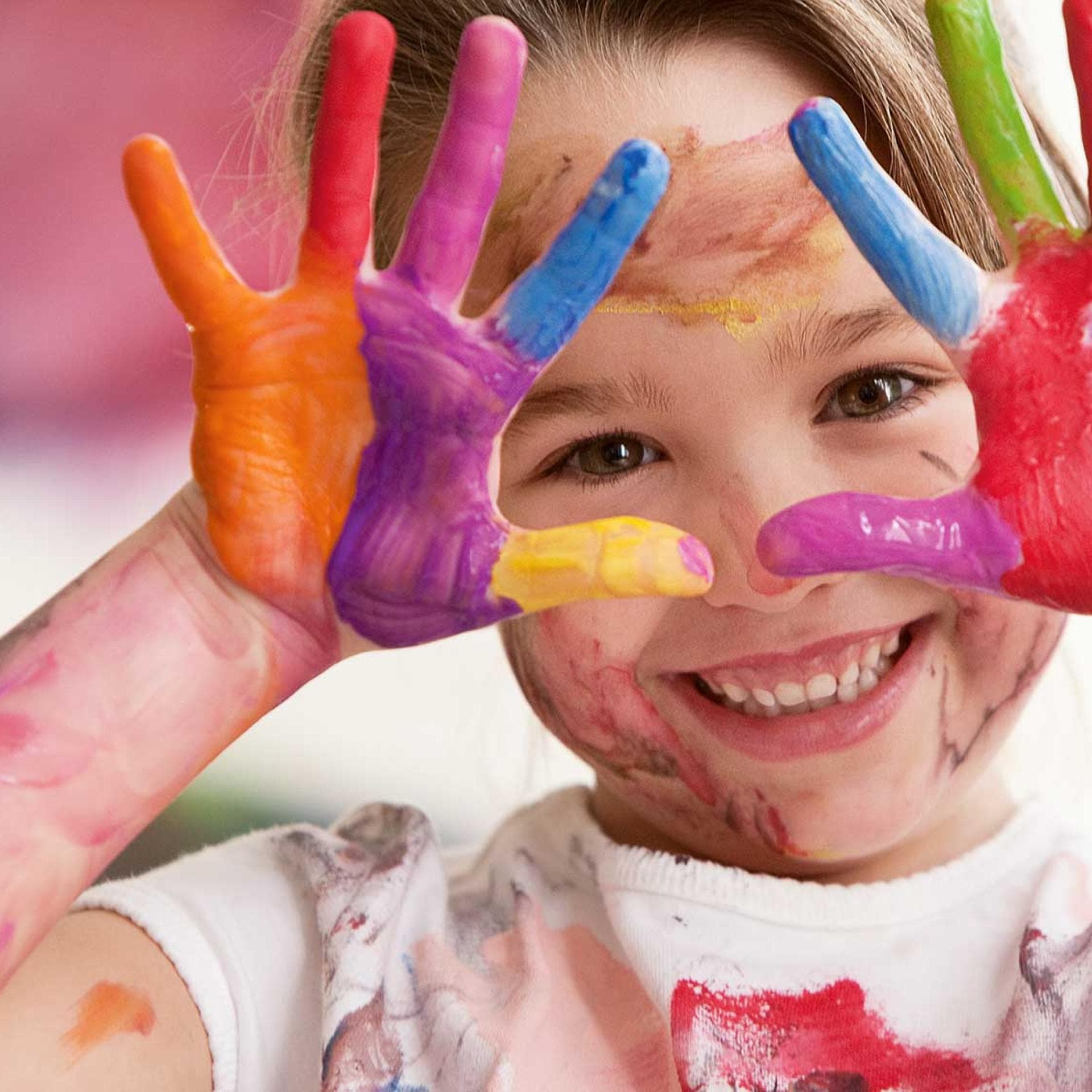 Fröhliches Kind mit bunten Fingerfarben an den Händen.