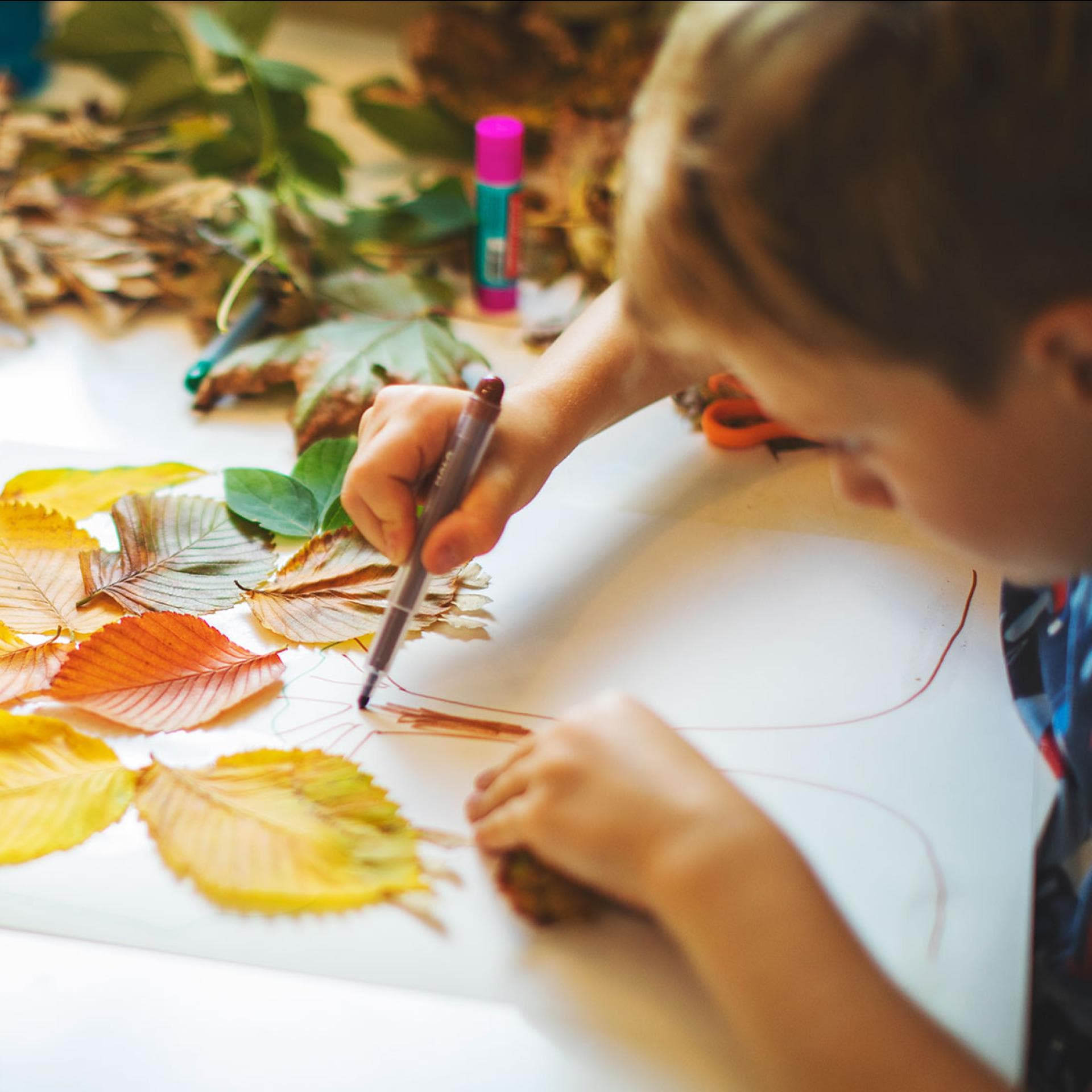 Kinder basteln mit Herbstblättern und Stiften.