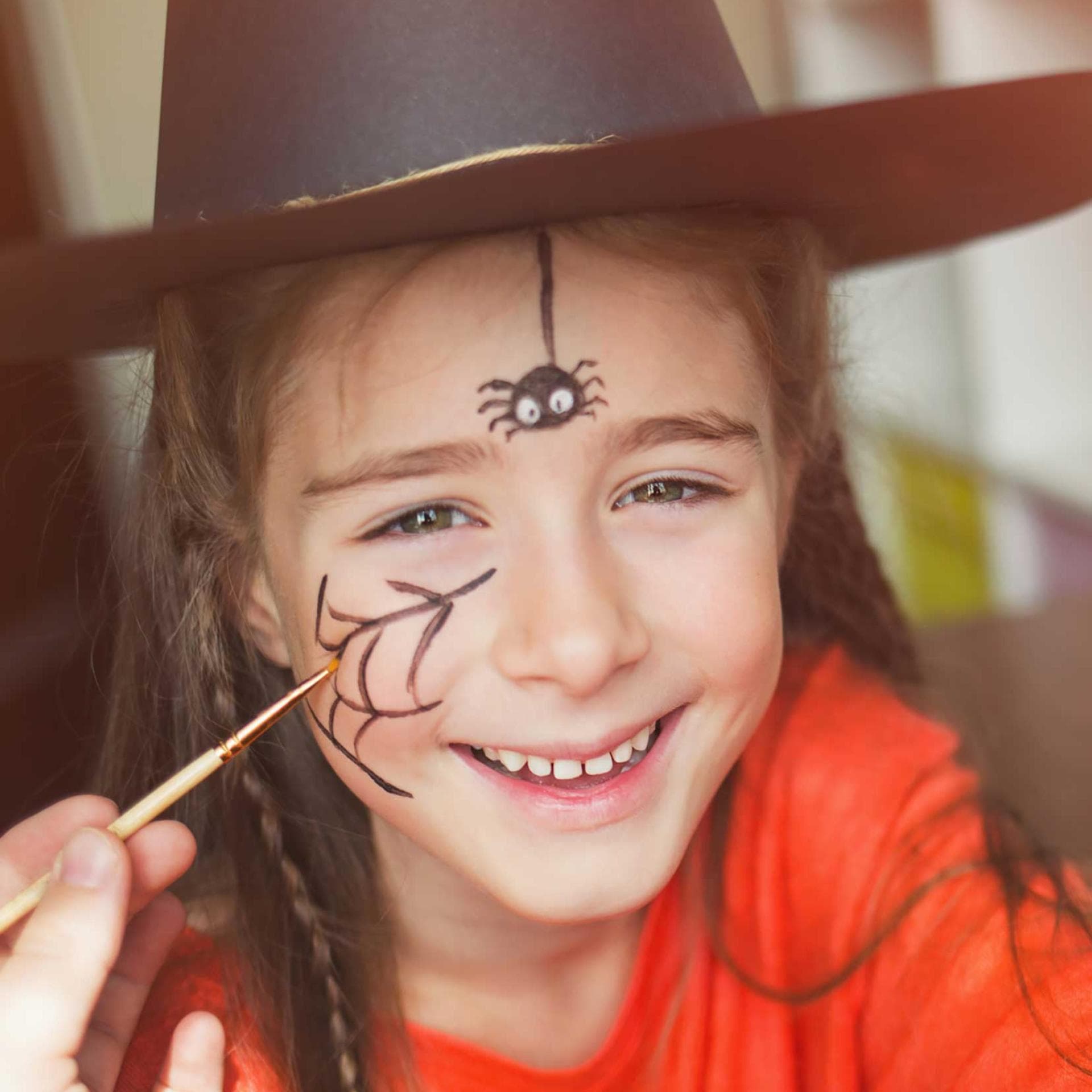 Mädchen mit geschminktem Spinnennetz auf der Wange und einer Spinne auf der Stirn.