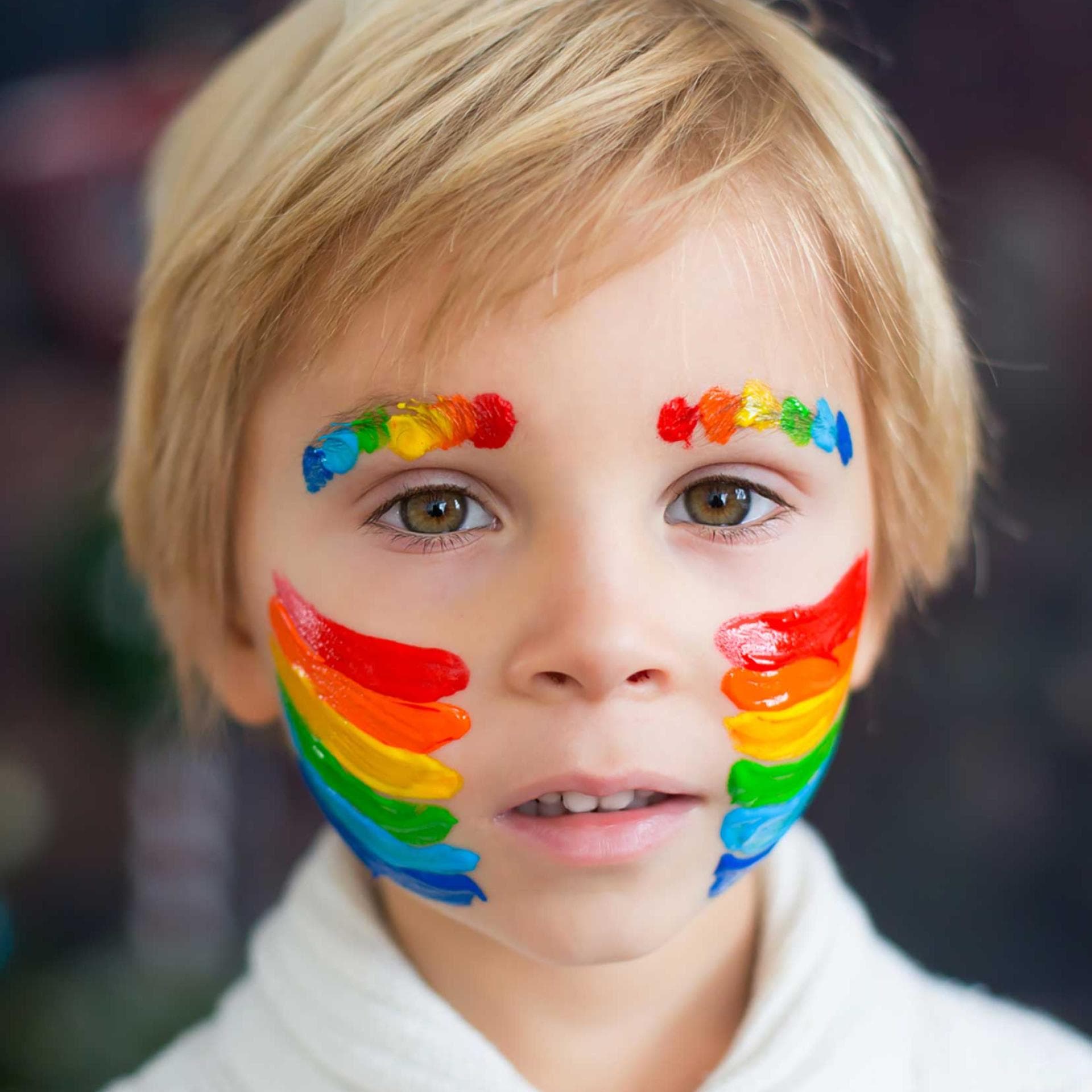 Junge mit geschminktem Regenbogen auf Wangen und Augenbrauen