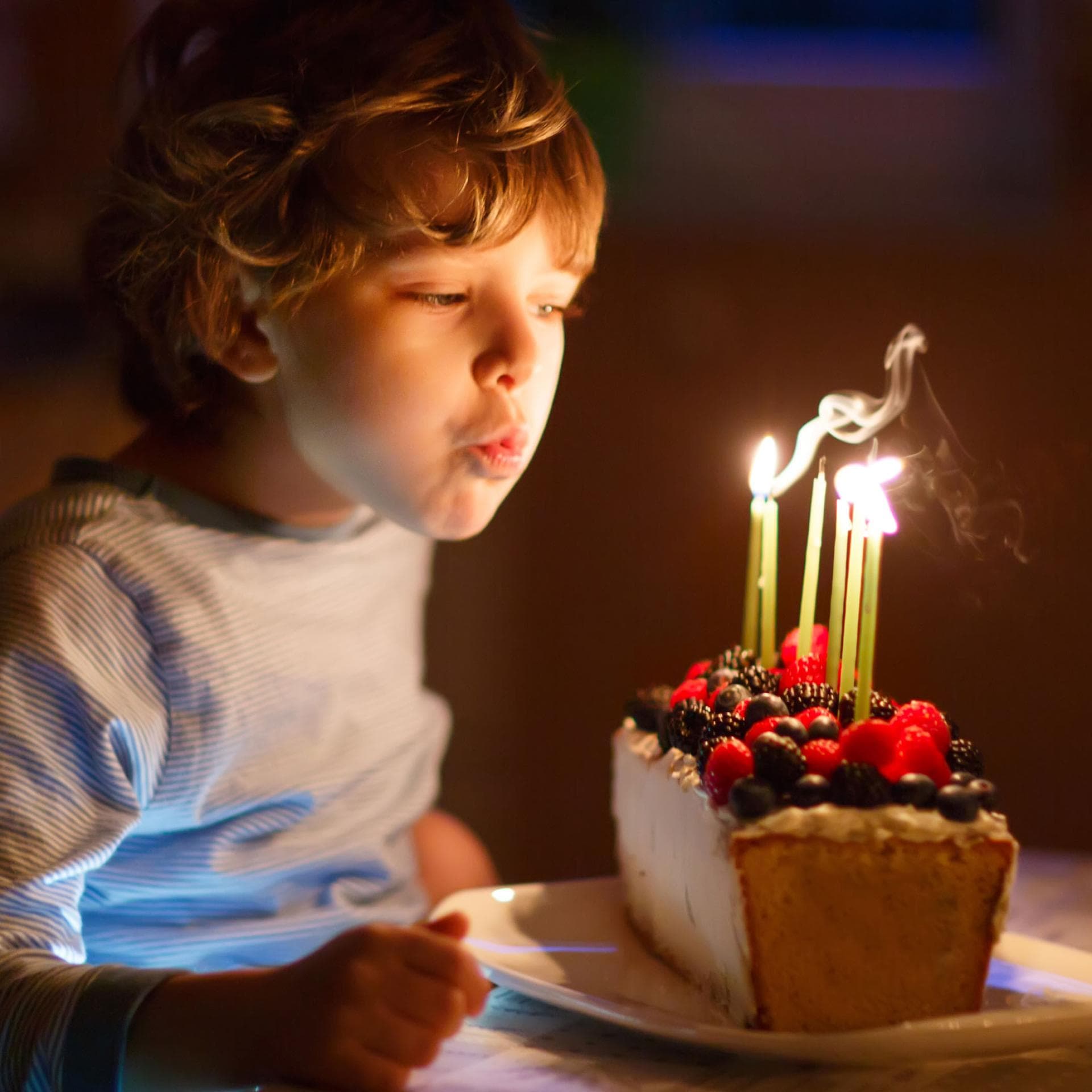 Kind pustet Kerzen auf Geburtstagskuchen aus.