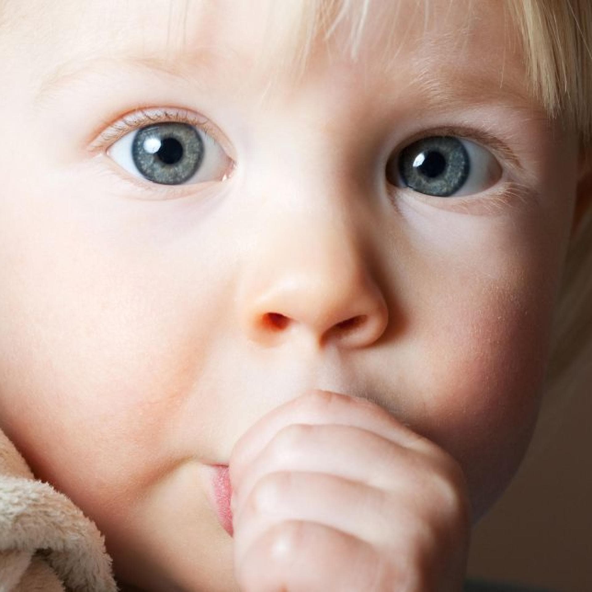 Kleines Kind nuckelt mit großen Augen am Daumen.