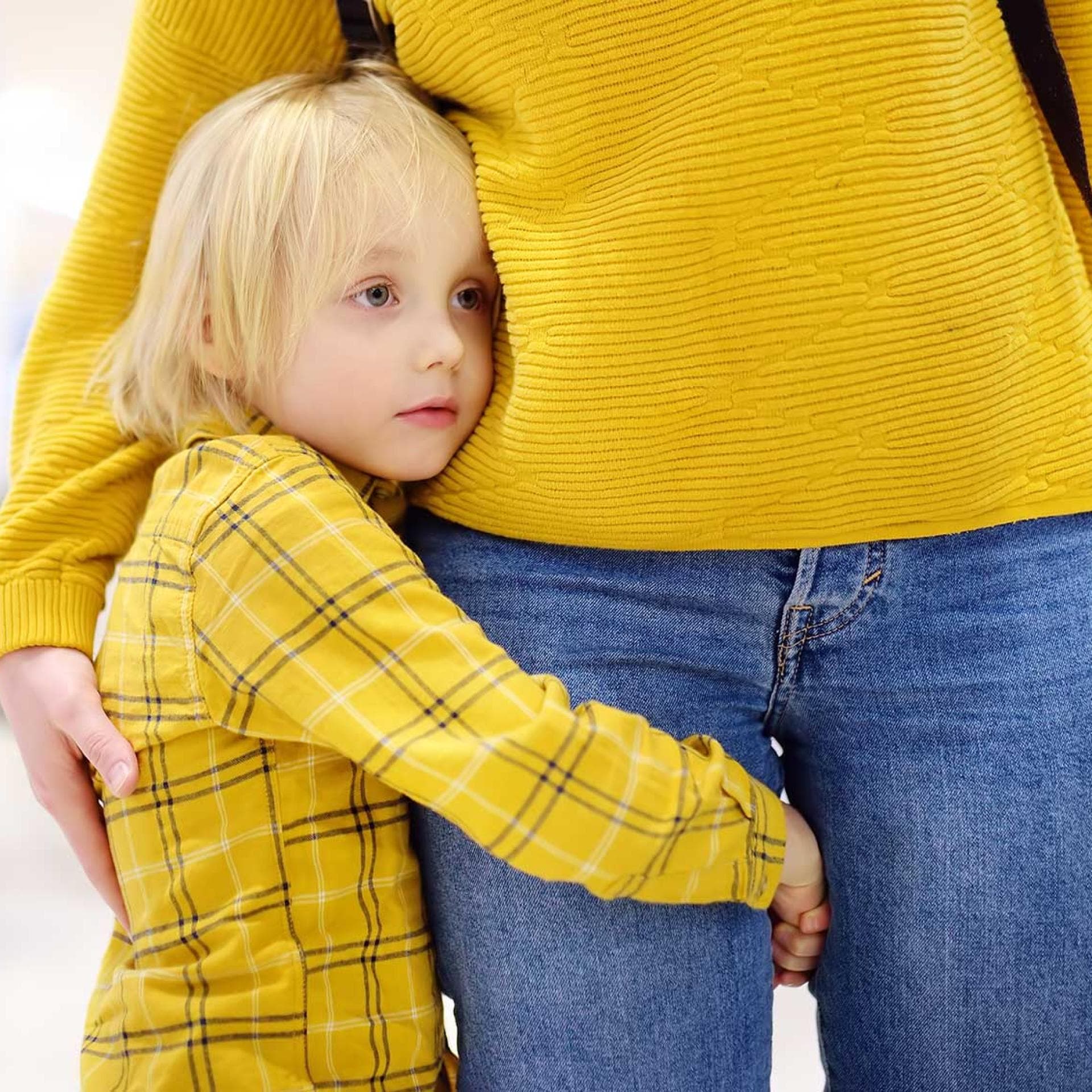 Kind umarmt das Bein seiner Mama, um ganz nah bei ihr zu sein