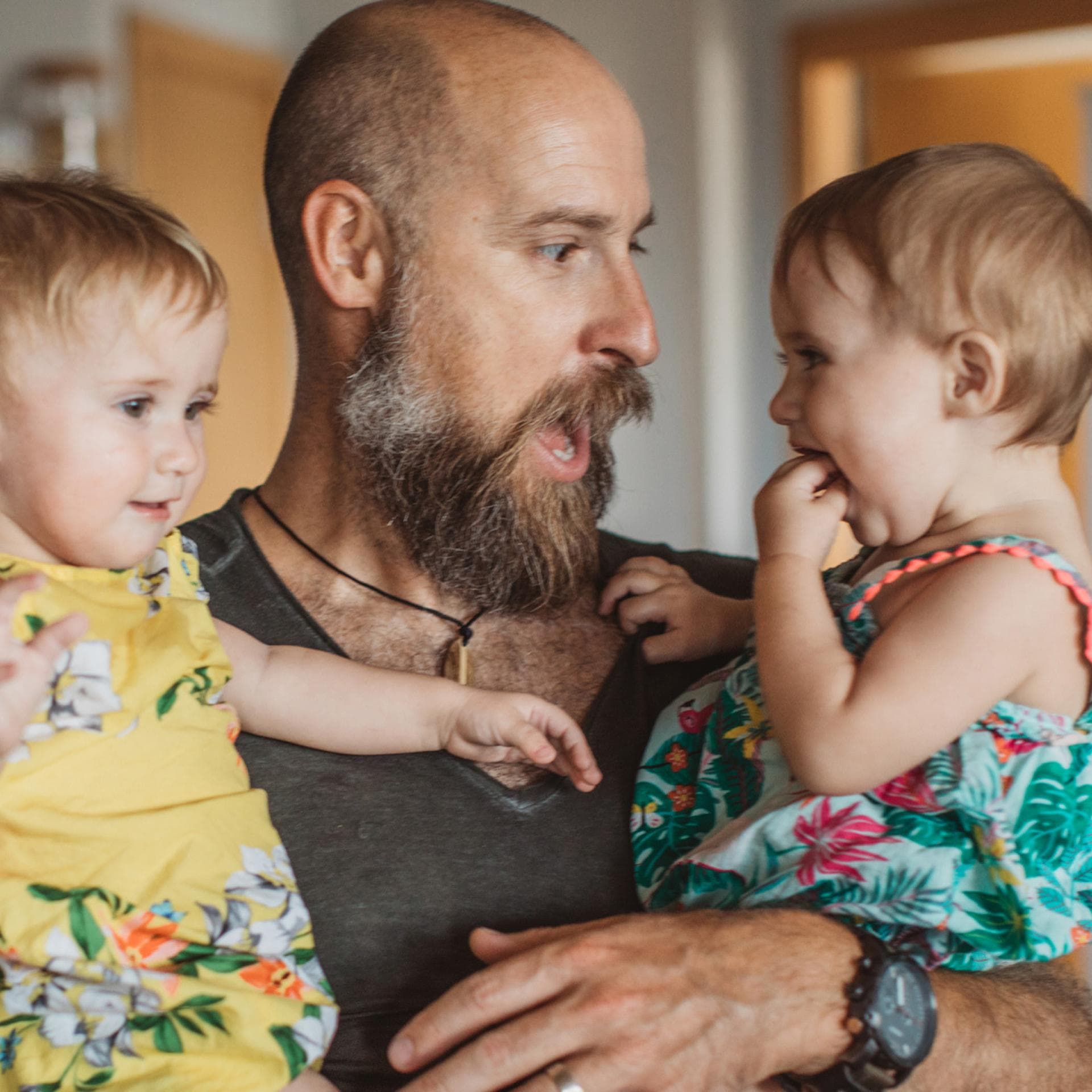 Papa mit Vollbart hat zwei Kinder auf dem Arm.