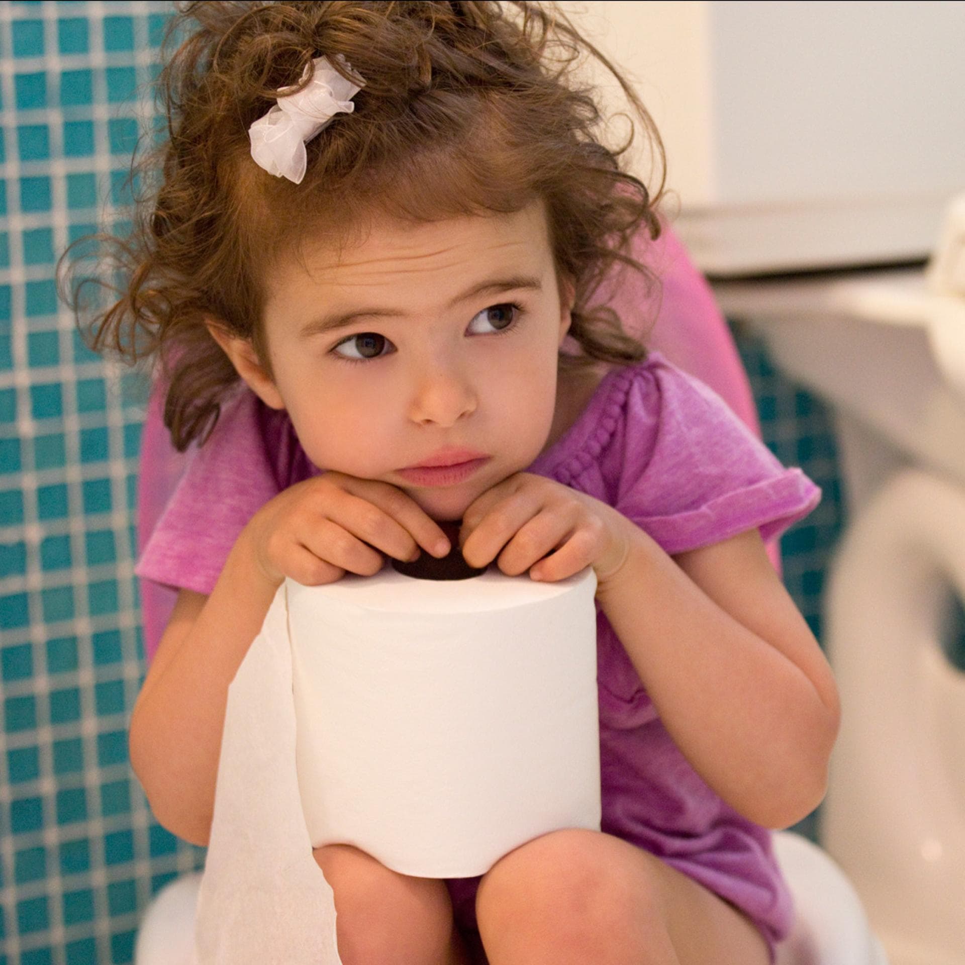 Ein kleines Mädchen sitzt auf der Toilette und schaut unglücklich. 