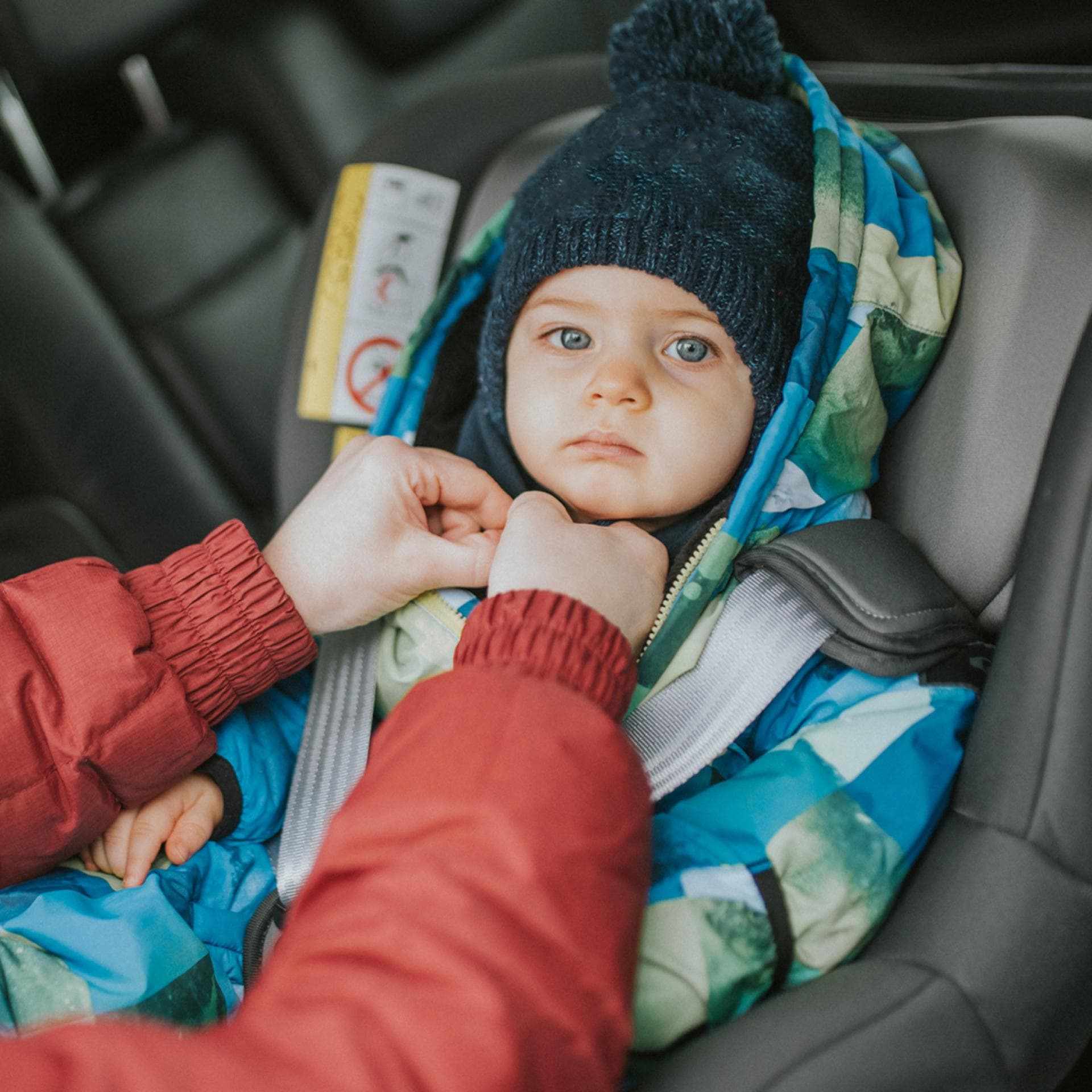 Frau schnallt Baby im Autokindersitz an.