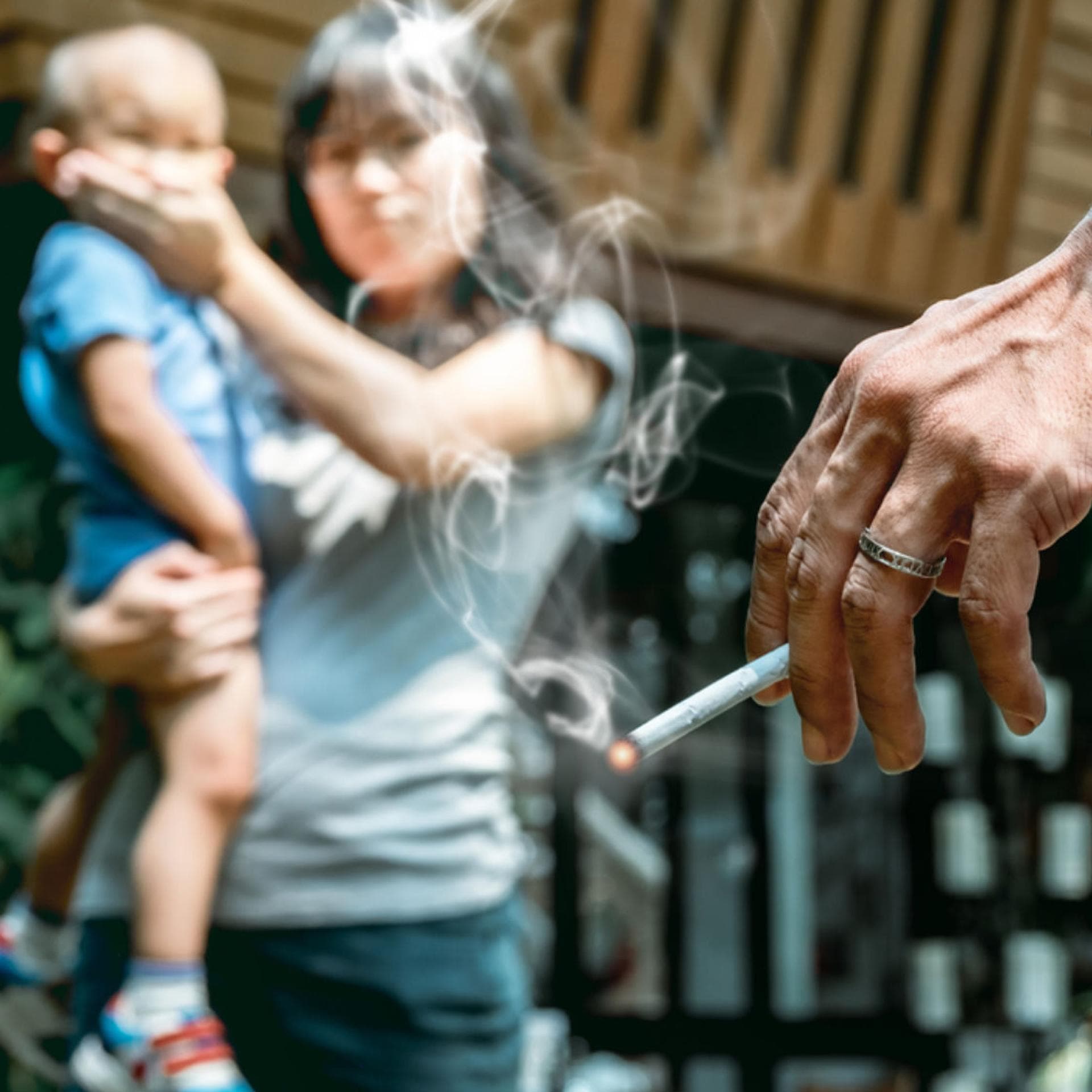 Eine Oma raucht vor einem Baby. Die Mutter hält ihm den Mund zu. 
