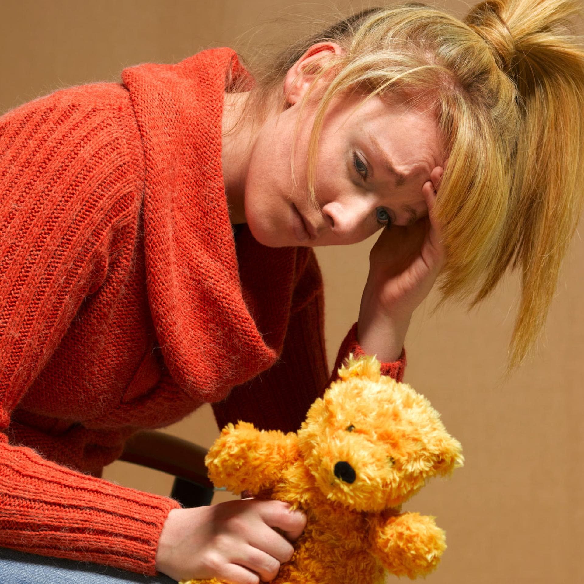 Erschöpfte, mutlose Frau mit Teddy in der Hand.