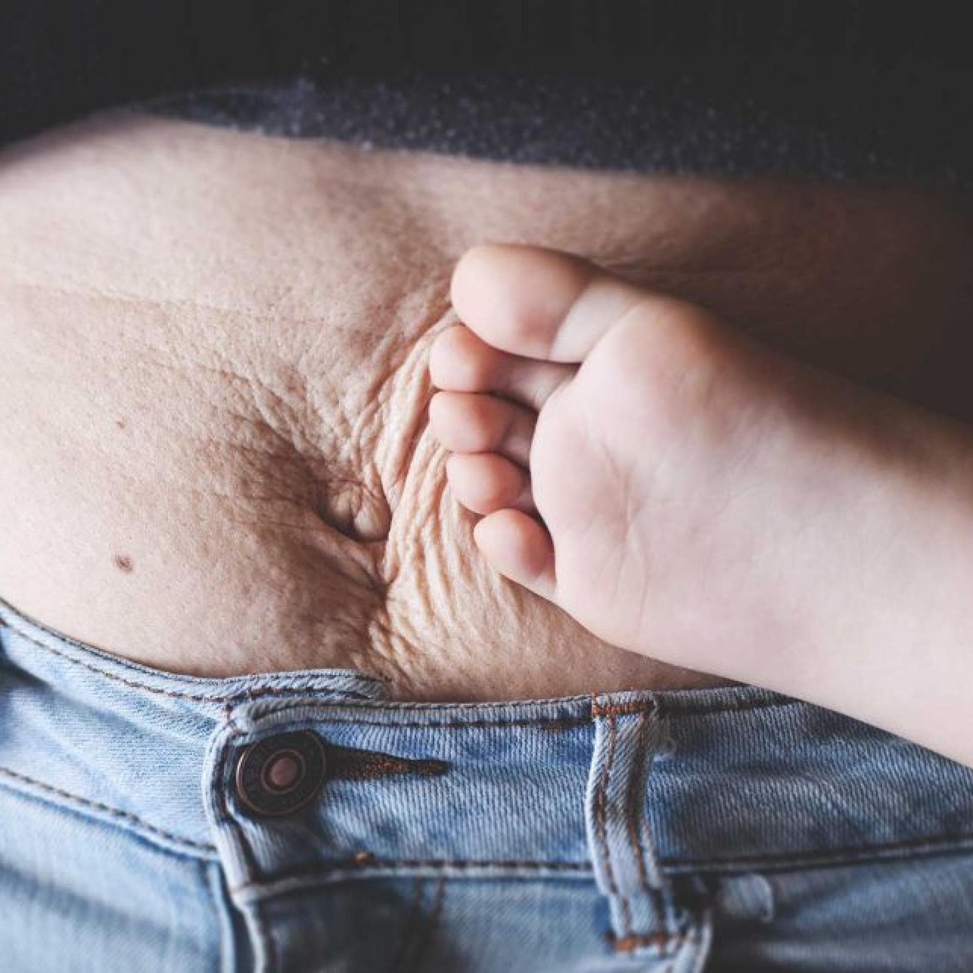 Kinderfuß an faltigem Mama-Bauch.