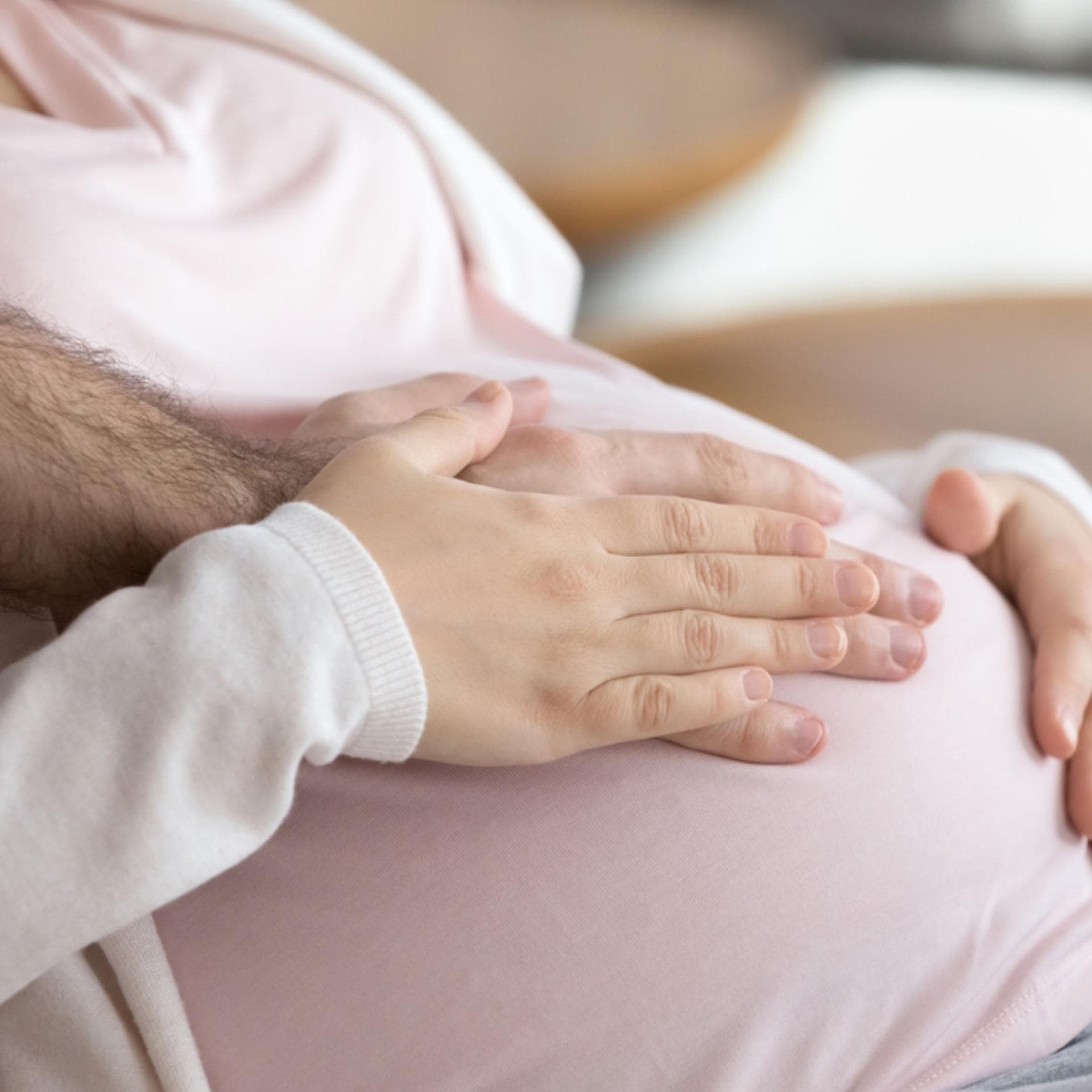 Frau und Mann legen Hände auf Babybauch.