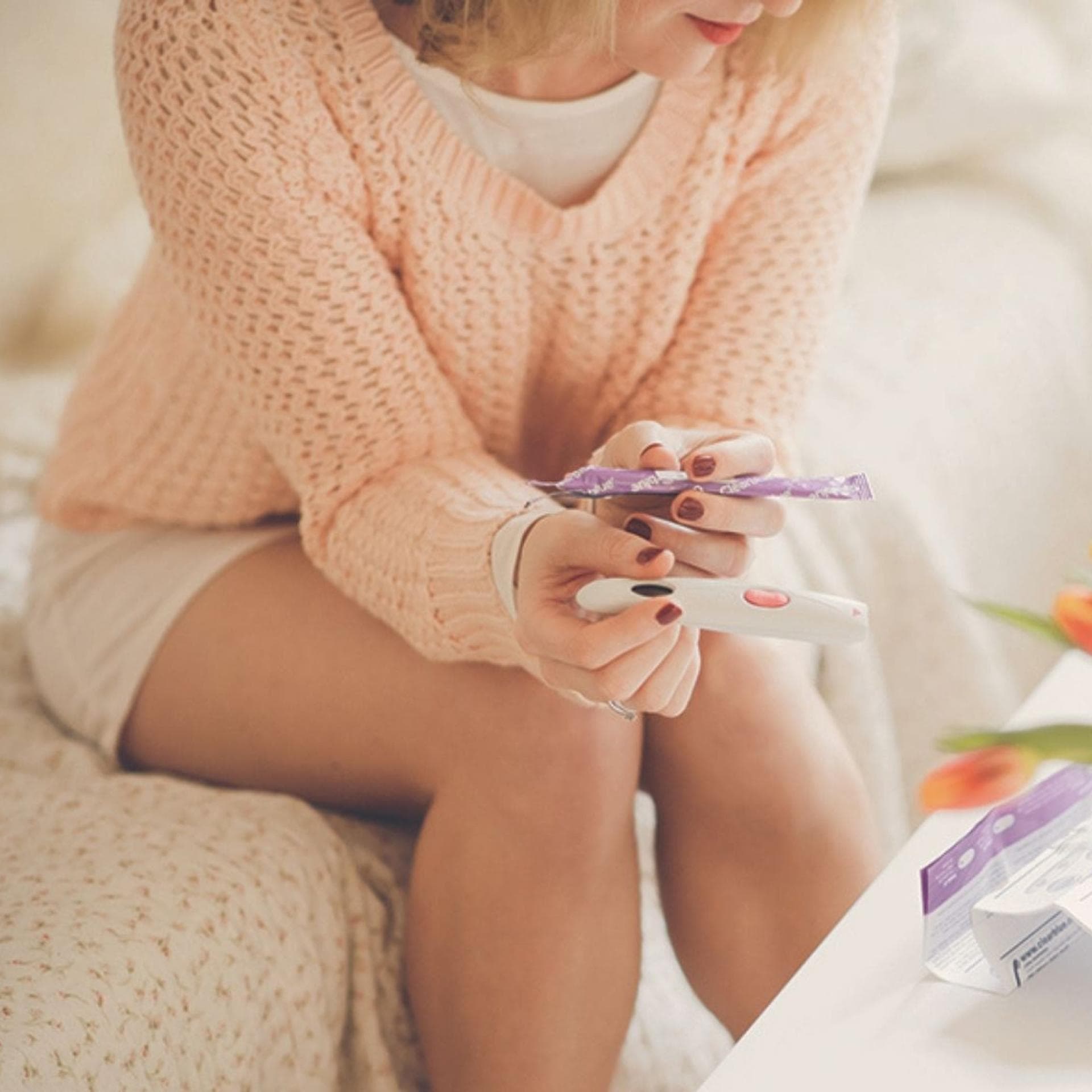 Frau sitzt vor Blumenstrauß mit Ovulationstest in der Hand.