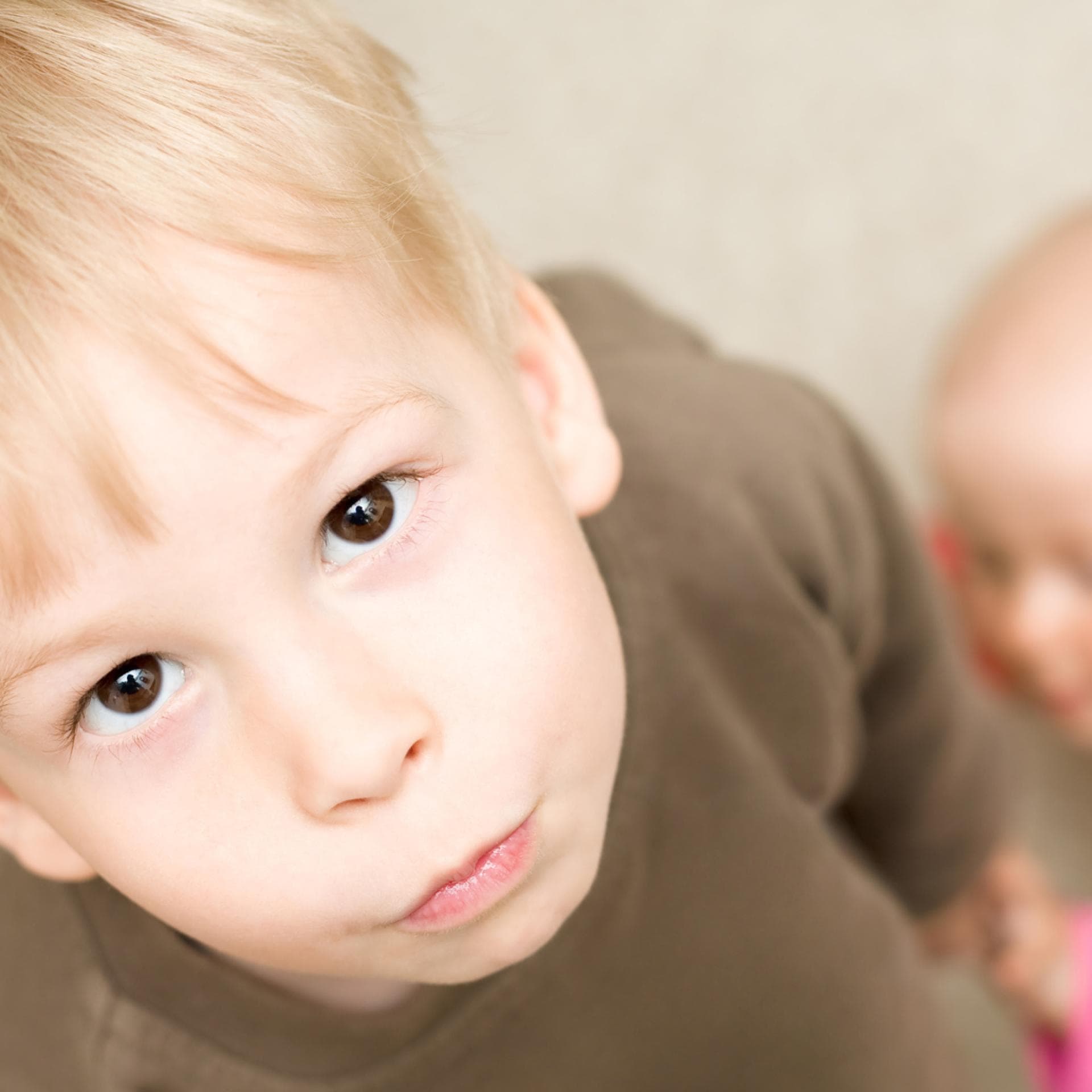 Ein kleiner Junge schaut genervt, während ein Baby sich an ihm hochzieht.