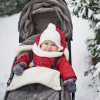 Ein kleines Mädchen sitzt dick eingepackt im Kinderwagen, der im Schnee steht.