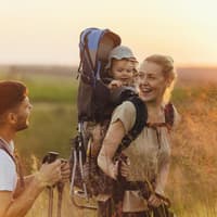 Eine Frau trägt ihr kleines Kind beim Wandern in einer Kraxe. 