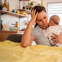 Junge Mutter mit Baby auf dem Arm fasst sich an den Kopf
