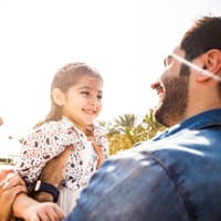 Mutter und Vater halten ihre lachende Tochter.