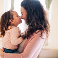 Eine Mutter trägt ihre kleine Tochter mit Schleife im Haar auf dem Arm.