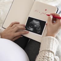Eine schwangere Frau schreibt in ihr Baby-Tagebuch und zeigt ihr Ultraschallbild.