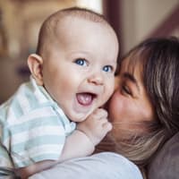 Ein Baby liegt lachend auf seiner Mutter.