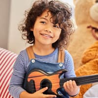 Ein Junge mit dunklen Locken sitzt mit seiner Gitarre im Kinderzimmer.