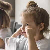 Mädchen sitzt mit Ellenbogen aufgestützt am Tisch und sieht wütend aus