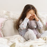 Mädchen sitzt im Schlafanzug auf dem Bett und weint