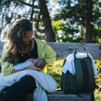 Eine Frau, die ihr Baby auf einer Bank im Grünen stillt.
