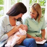 Mutter füttert ihr Baby, Mütterpflegerin sitzt daneben