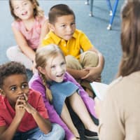 Kindergartenkinder hören einer Erzieherin beim Vorlesen zu