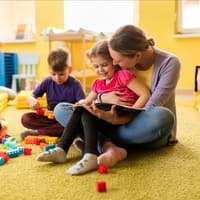 Erzieherin liest einem Vorschulmädchen ein Buch vor und beide lächeln