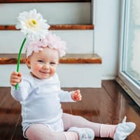 Ein kleines Mädchen lacht und hält eine Blume in der Hand. 