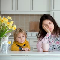 Mama sitzt müde am Tisch, Kind ist hellwach