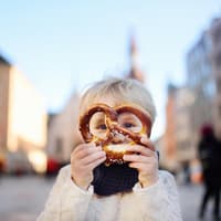 Ein kleiner Junge hält sich eine Brezel vor das Gesicht.